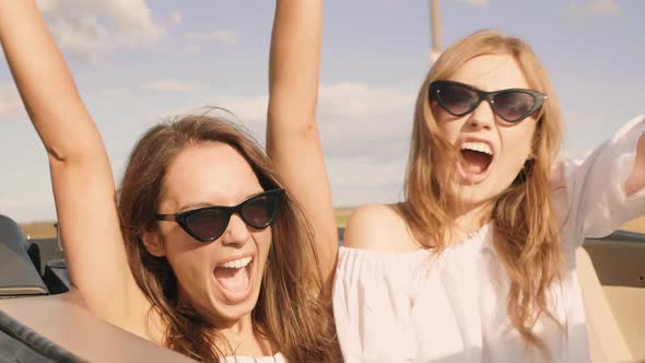 Two young beautiful and smiling hipster female in convertible car