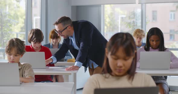 Diverse Teenage Students Working on Laptop in Classroom and Mature Teacher Help