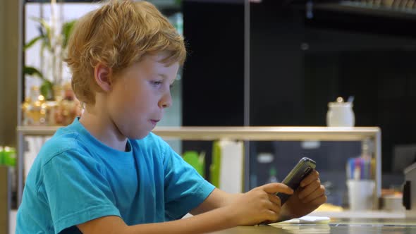 Blonde boy uses smartphone while surfing the internet in cafe