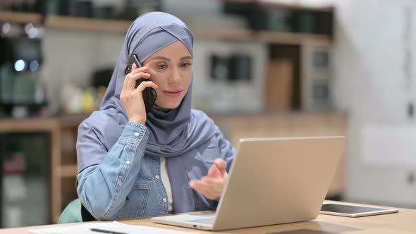 Arab Woman with Laptop Talking on Smartphone at Work 