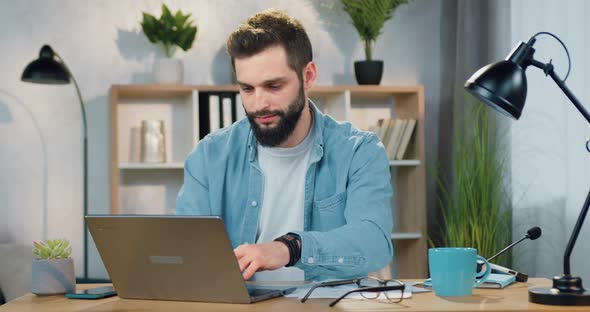 Man Sitting at his Workplace at Home and Writing Down Notes from Computer Screen Into Paper report
