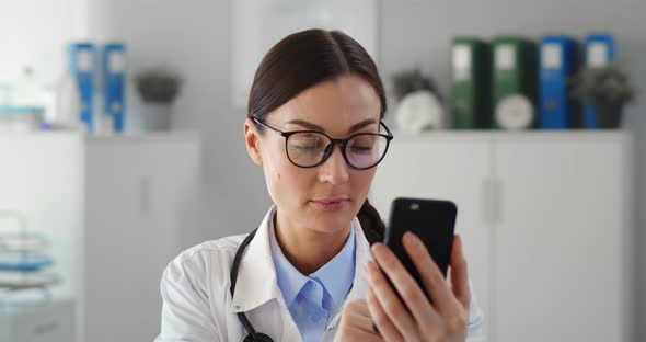 Happy Female Doctor Using Smartphone in Medical Office