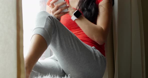 Woman sitting on windowsill and using mobile phone