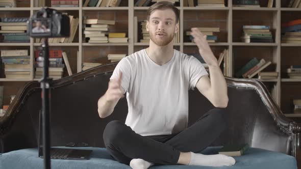 Positive Millennial Blogger Recording Video About Literature in Library. Portrait of Young Handsome