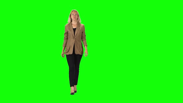 Blonde Girl in a Stylish Brown Jacket, Black Trousers and High-heeled Shoes Going Against a Green