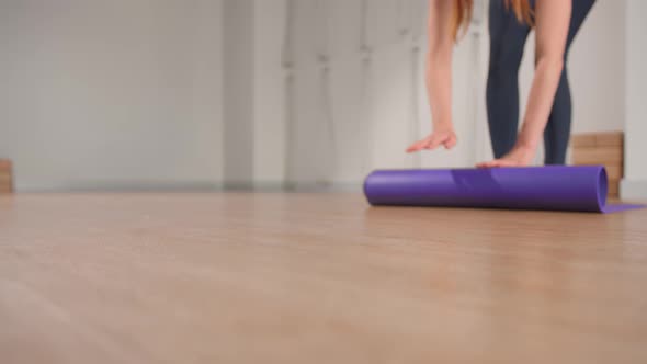 Woman spreading yoga mat after training in studio. Girl folding fitness mat on floor at yoga studio