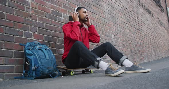 Mixed race man sitting on skateboard and listening to music in the street