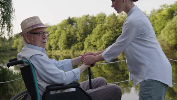 Man Sit in a Wheelchair and Nurse Huddle His Hands