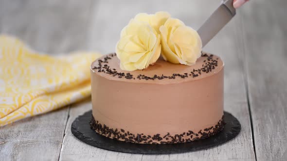 Cutting of chocolate cake on plate. Chocolate cake decorated white chocolate flowers.	