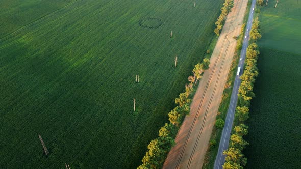 Drone Flying Over Road Between Green Agricultural Fields During Dawn Sunset