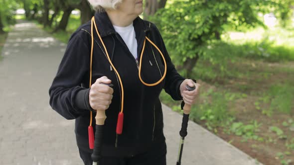 Active Senior Old Woman Training Nordic Walking with Ski Trekking Poles in Park