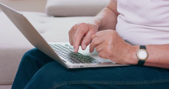 A Senior Man Types on the Keyboard of His Laptop