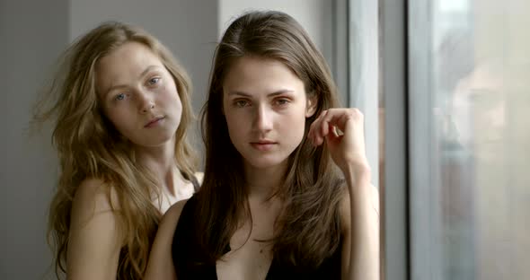 Two Sexual Women Are Posing in Front of Camera, Standing Near Windows with Daylight