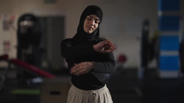 Medium Shot Portrait of Confident Slim Middle Eastern Sportswoman Warming Up Muscles Indoors in Gym