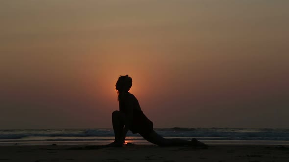 Man stretching at sandy beach in Goa at sunset.