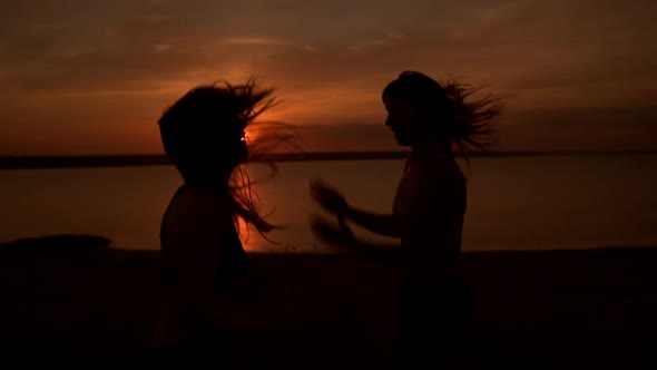 Silhouettes of Two Beautiful Girls Dancing Zumba in Field at Sunrise