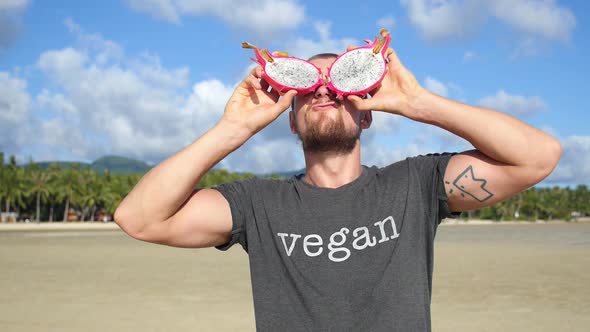 Funny Bearded Man in Vegan T-Shirt With Dragon Fruit Pitaya Eyes on Beach
