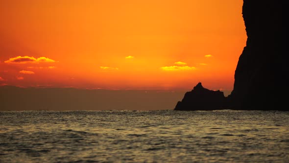A Red Burning Sunset Over the Sea with Rocky Volcanic Cliff