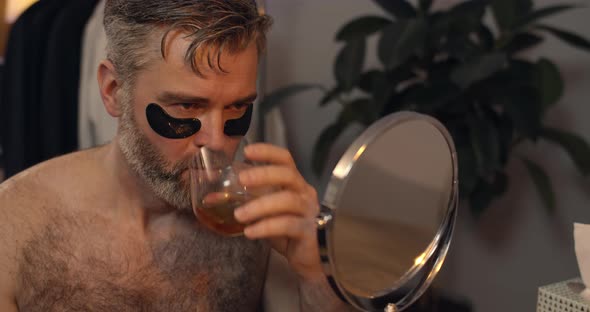 Mature Man Making Painful Facial Expression While Plucking Eyebrows in Front of mirror.Bearded