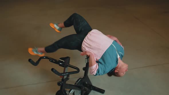 Athletic Girl Make Acrobatic Trick on Bike Exercising Workout on Stationary Cycling Machine Indoors