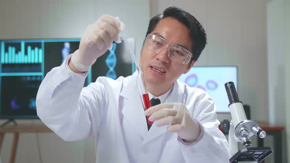 Young Asian Male Research Scientist Holding Glass Test Tube And Speaking To The Camera