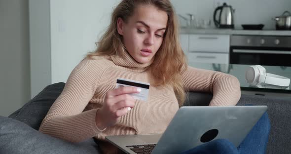 Blonde Woman in a Beige Sweater Shopping on the Internet and Pay Bill By Credit Card with Laptop at