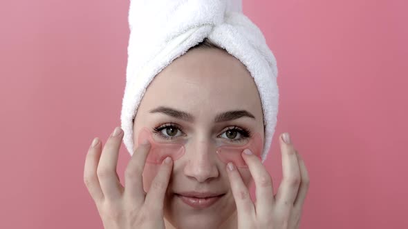 Plesant nude girl applying collagen eye masks on face in front of a mirror