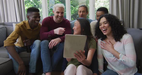 Diverse group of happy male and female friends looking at tablet and laughing in living room