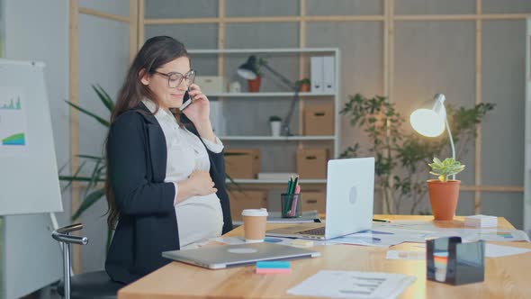 A Beautiful Pregnant Woman Talking on a Cell Phone Sitting at a Table