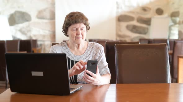 Happy Senior Woman Using Phone And Laptop At The Coffee Shop