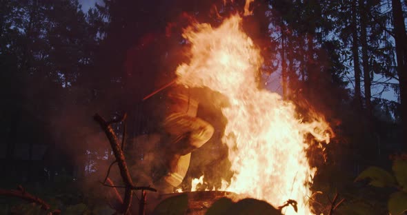 Fire Fighter with Safety Equipment and Axe Extinguishing Fire in Forest at Night