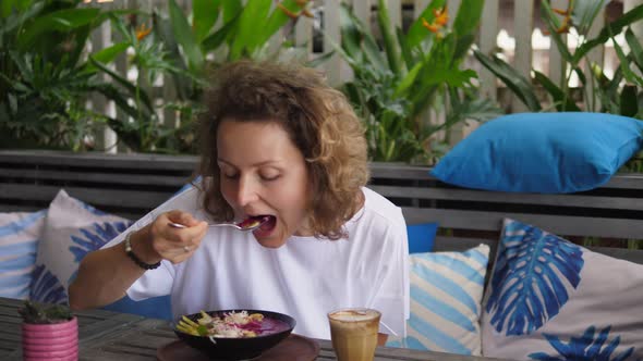 Caucasian Girl Eating Her Tropical Smoothie Bowl with Great Pleasure in an Outdoor Restaurant