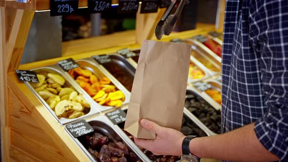 Man is Buying Healthy and Sweet Dried Pear in Grocery Shop or Market Taking Fruit Secs in Paper Bag