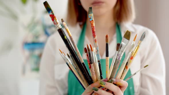 Female Artist in an Apron Holds Lot of Brushes in Hands Closeup