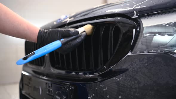 Close-up of Man Hand in Black Protective Gloves Cleaning Radiator Grille with Special Brush. Carwash