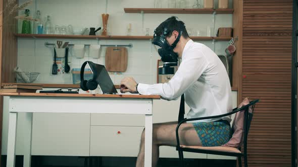 A Man in a Hazmat Mask Is Operating a Laptop in the Kitchen. Lockdown Concept, Coronavirus Pandemic.