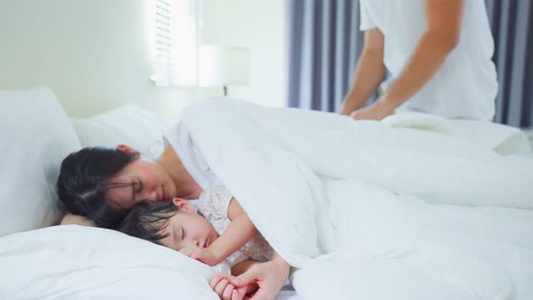 Attractive man father put blanket on comfortable sleeping little baby kid and asleep mother on bed.