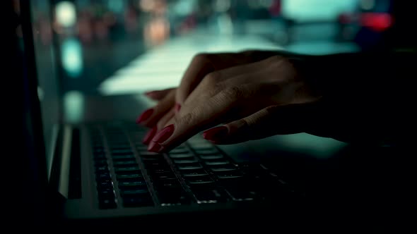 A Woman Works on a Laptop at Home on a Blurred Background of a Working TV