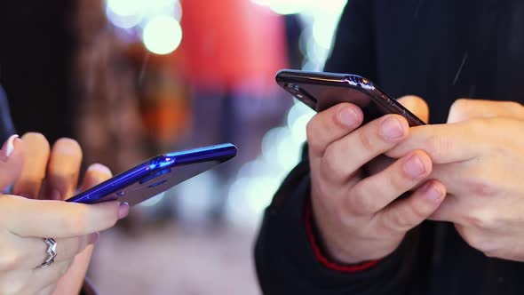 Close Up Hand of Man and Woman Uses Mobile Phone in Snowy Evening Chatting with Friends