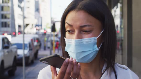 African american woman wearing face mask talking on smartphone in street