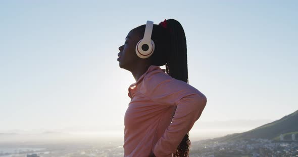 African american woman exercising outdoors putting on wireless headphone in countryside at sunset