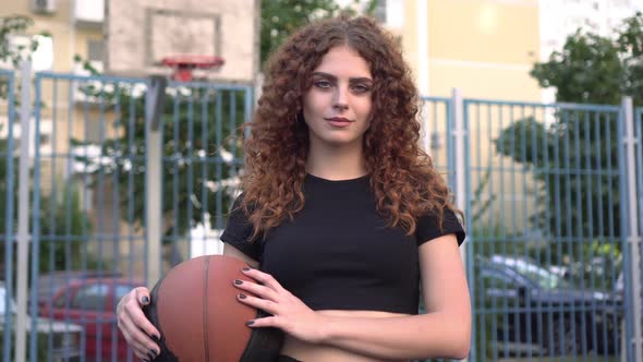 Beautiful Woman with Curly Hair and a Ball on a Sports Basketball Court