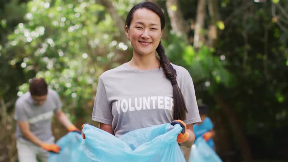 Smiling asian woman wearing volunteer t shirt holding refuse sack for collecting plastic waste