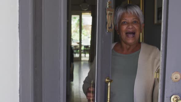 Smiling senior mixed race woman opening front door and welcoming