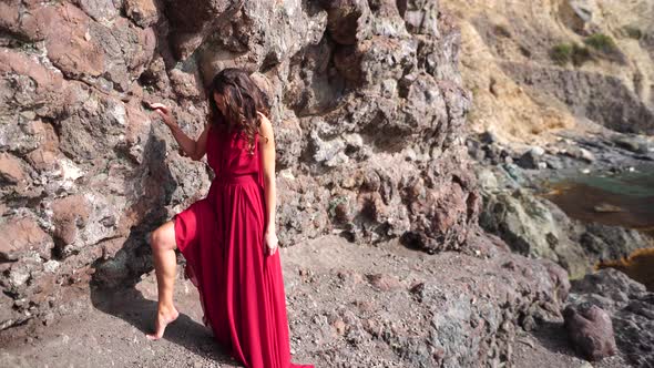 Side View a Young Beautiful Sensual Woman in a Red Long Dress Posing High Above the Sea on a