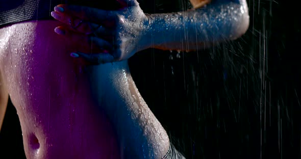 a Woman with Pink Hair and a Black Swimsuit Stands in the Rain in the Dark. She Runs Hand Over Her