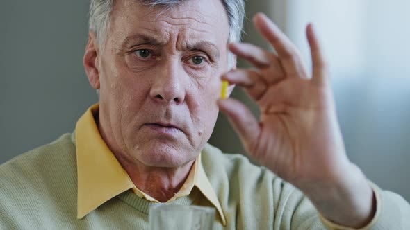 Portrait Closeup of Elderly Man Holding Pill Sad Grandfather Look at Capsule Serious Mature Old