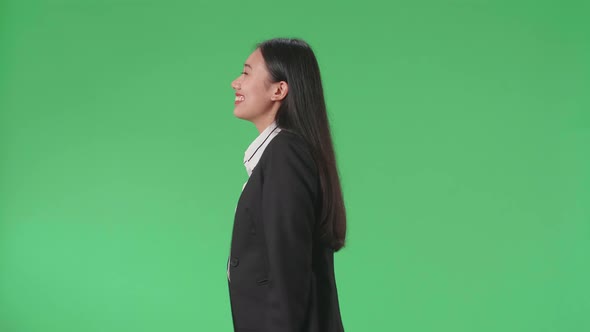 Side View Of A Smiling Asian Business Woman Walking Through Green Screen In The Studio