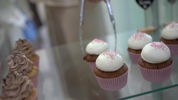 Seller taking cupcake from display in confectionery shop