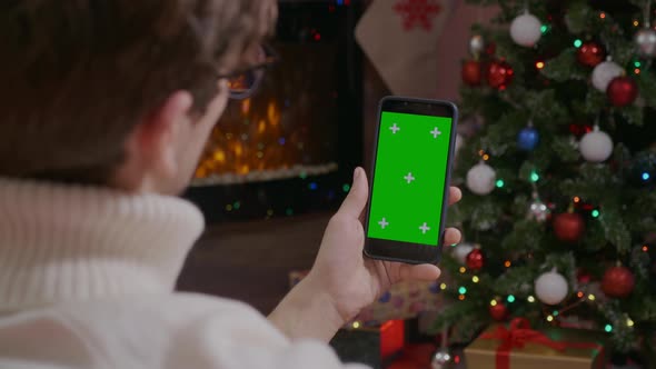 Handsome Man holding smartphone with Green Screen on Christmas background with gifts.